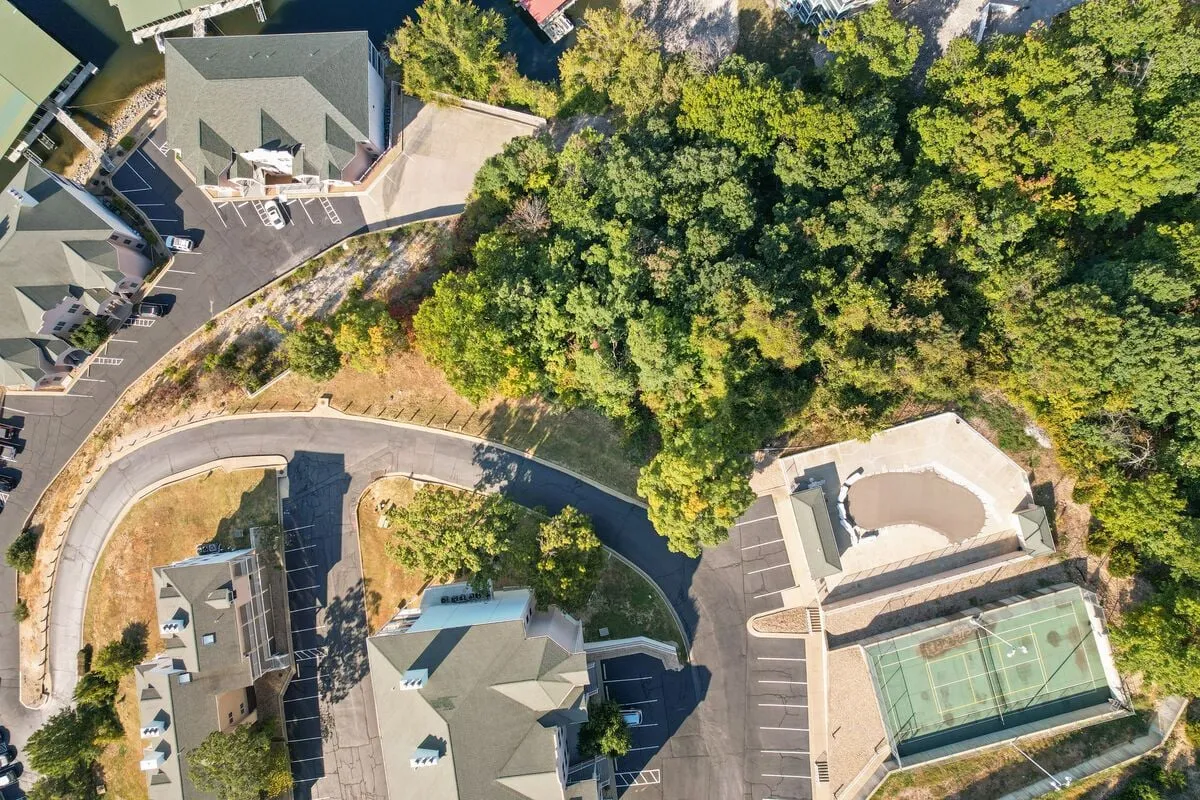 A basketball court surrounded by dense greenery and a curved road, set within a relaxed community area. The outdoor space feels open, communal, and ideal for friendly games or family tournaments.