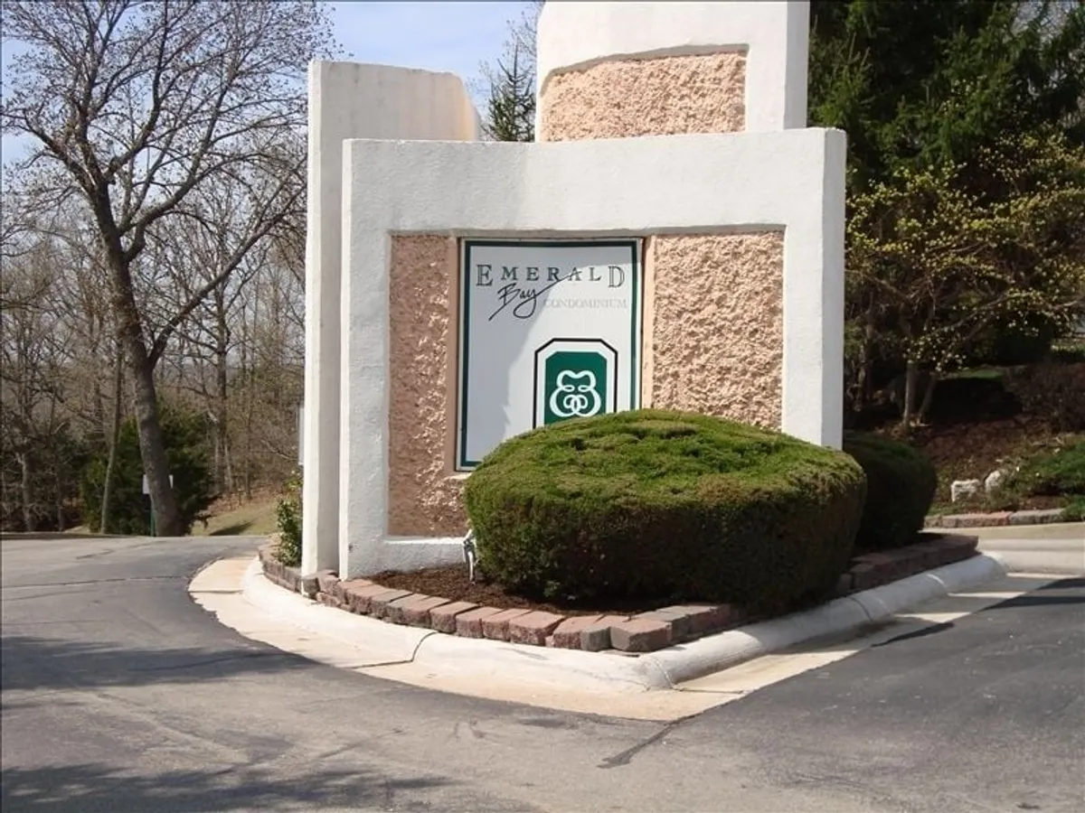 The entrance to the Emerald Bay community is marked by a welcoming sign, manicured bushes, and a paved entranceway. The scene captures the start of an exploration, inviting visitors to venture further.