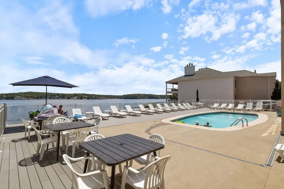 A spacious swimming pool and patio seating overlook a stunning lake view, with the water stretching out in the distance. The scene suggests leisure and relaxation, with opportunities for both socializing and quiet reflection by the water.