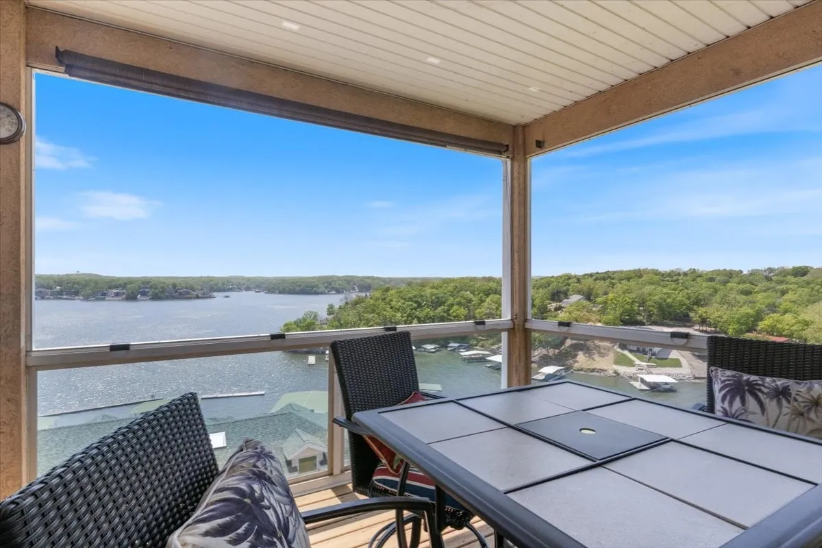 This image captures an outdoor dining table set on a balcony or patio, with an expansive view of the lake and lush greenery in the background. The scene invites thoughts of quiet mornings or relaxing evenings spent enjoying the tranquil surroundings and panoramic water views.