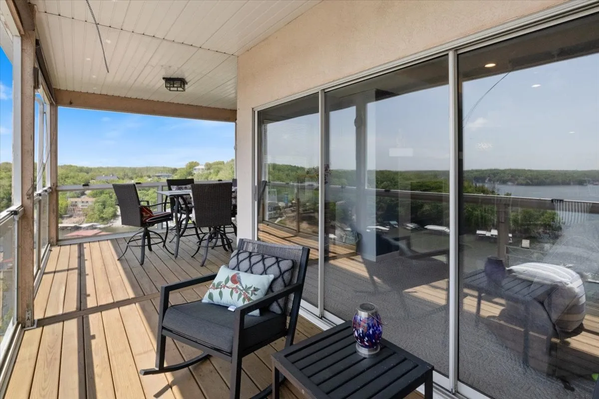 This exterior image shows an outdoor seating area and dining table set on a deck, with a clear, expansive lake view in the background. The arrangement suggests both high-top dining and lounge seating, perfect for gatherings and relaxation. The tranquil scene hints at an elevated vantage point, offering beautiful views over the main channel.