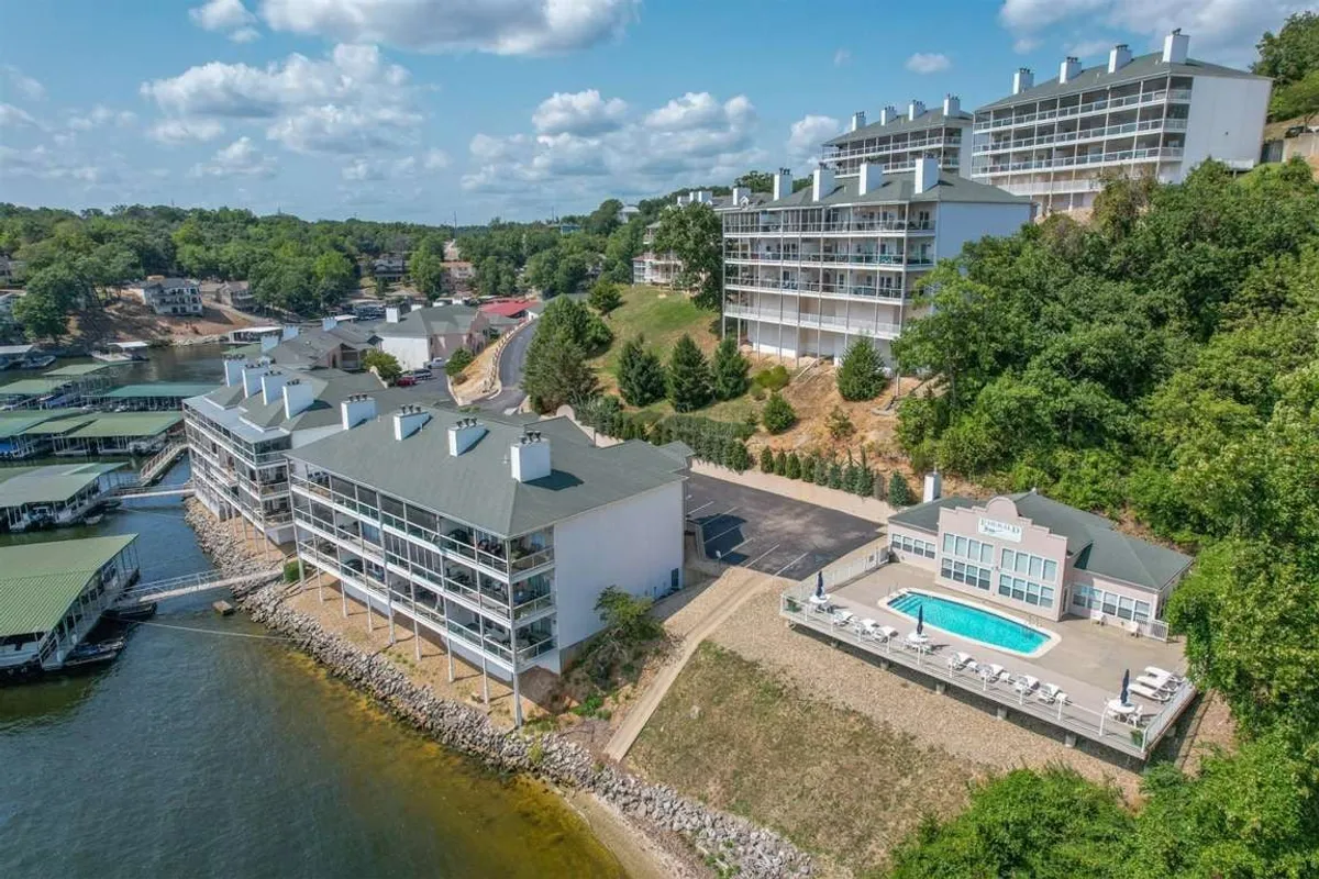 This image captures a stunning lakefront property with a swimming pool set amidst landscaped gardens and lush greenery. The scene includes the pool area, the lake's edge, and a backdrop of natural beauty, evoking a sense of relaxed, resort-like leisure.